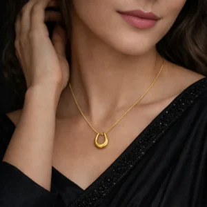 Gold-toned horseshoe pendant necklace on a sleek snake chain displayed on black fabric.